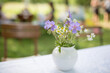 ein Sträußchen aus Wiesenstorchschnabel ( Geranium pratense ) in einer weißen Vase, auf einem mit einem Gartentisch mit weißem Tischtuch