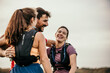 © La Famiglia - Side view of a group of runners wearing race gear and hugging after a race. They are all smiling and laughing and look happy to be there together