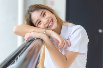 Beautiful and pretty young Asian girl student in Thai university student uniform smiling confidently and looking at camera in university background