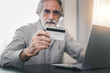 © butsaya33 - Senior elderly grey haired moustache bearded man using credit bank card and laptop transferring money purchases online shopping. People lifestyle concept.