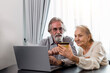 © butsaya33 - Happy Caucasian 70s mature couple using credit bank card and laptop transferring money purchases online shopping. Senior man and woman surfing the internet. Modern retired lifestyle people.