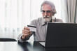 © butsaya33 - Senior elderly grey haired moustache bearded man using credit bank card and laptop transferring money purchases online shopping. People lifestyle concept.