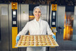A food factory worker is standing in front of the ovens and carrying cookies for baking.