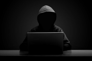Mysterious man wearing black hoodie using laptop in the dark room. Hacker and cyber security concept.