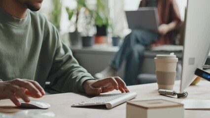 Medium close-up of developer sitting at his workplace with computer and typing on keyboard