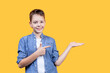 Portrait of a happy boy pointing to the right at copy space on his hand. He is smiling and looking at camera. Yellow background. Front view. Suitable for collage and banner making and other design