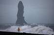 Brave girl in yellow raincoat admires powerful very high waves during storm on famous reynisfjara black sand beach, Iceland. Troll toes on the background