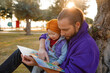 Dad and baby read a book under a tree in the park.