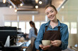 © Supachai - Female barista in apron smiling and serving cup of hot coffee to client in coffee shop. Barista owners small business.