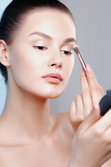 Wall Mural - Young beautiful woman with natural makeup looks in  mirror and applies eye shadow with brush