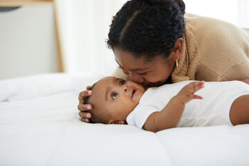 Wall Mural - African young mother kissing her infant baby lying on the bed