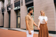 © dikushin - Cheerful young couple in love standing holding hands on city street and looking on each. Handsome bearded man with tattoo and cute blonde woman walking drinking takeaway coffee enjoying time together.