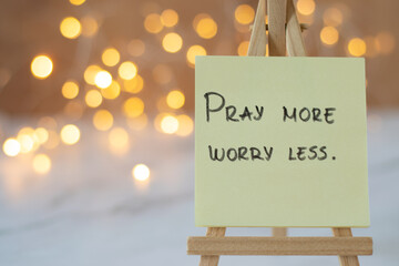 Pray more, worry less, handwritten message on note with blurred bokeh background. A closeup. Christian biblical text to trust and have faith in God and Jesus Christ.