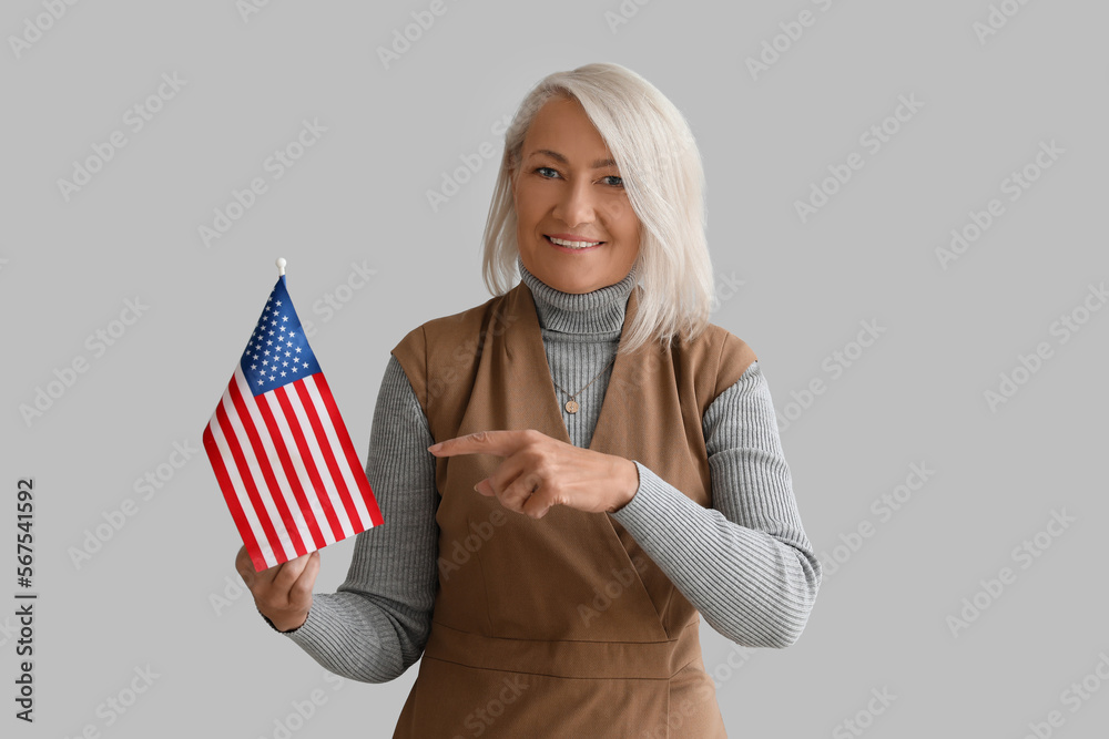 Mature woman pointing USA flag on grey background
