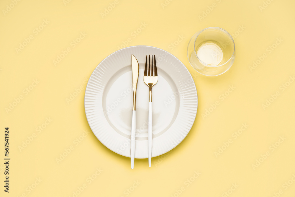 White plate with cutlery on yellow background