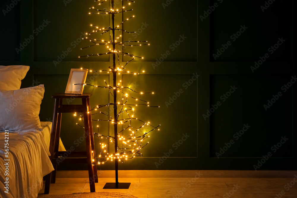 Bedside table with frame and glowing tree lamp in bedroom at night