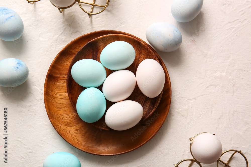 Wooden plate with beautiful Easter eggs on light background