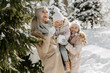 © andriychuk - Front view of mother with daughters enjoying winter day in forest. Loving mother standing near green tree with daughters and playing with snow during winter vacation