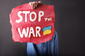 Wall Mural - Woman holding poster with words Stop the War on black background, closeup