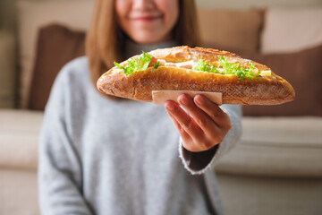 Wall Mural - Closeup image of a young woman holding a piece of french baguette sandwich at home