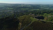 Establishing Drone Shot Over Back Of Cow And Calf Rocks Looking Over Valley With Ilkley Spa Town On Sunny Summer Day At Golden Hour West Yorkshire UK