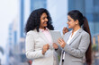 © G-images - Two businesswomen working on a tablet outdoors.