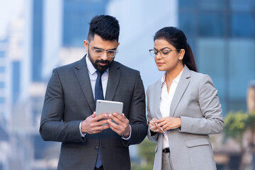 Indian businessman and businesswoman using digital tablet on city street.