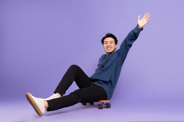 Wall Mural - Image of young Asian man playing skateboard on purple background