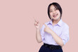 Happy pretty braces Asian school girl pointing finger to copy space isolated on pink background.
