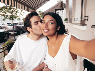 Smiling beautiful woman and her handsome boyfriend. Happy cheerful family. Sexy couple cheering with glasses of red wine at their date in restaurant. Drinking alcohol at veranda cafe. Taking selfie