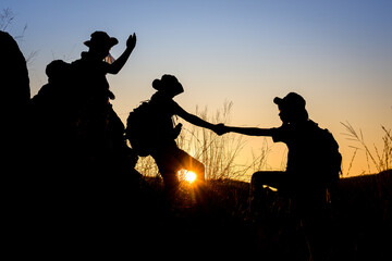 silhouette of Scout students showing help to each other Hold hands and pull each other up from the cliff to explore the beautiful forest in the evening as the sun sets.