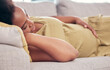 © T Mdlungu/peopleimages.com - Pregnant, maternity and sleeping woman resting holding her tummy or stomach and relax expecting a baby. Home, pregnancy and lying on a couch or sofa in a house or apartment on a break in a lounge