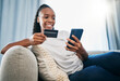 © Lou W/peopleimages.com - Credit card or black woman with phone for online shopping or payment, internet purchase or ecommerce in living room. Fintech, happy or girl on smartphone for trading, banking or invest on home sofa