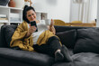 © cherryandbees - young adult smiling woman relax on sofa at home using mobile phone drinking coffee
