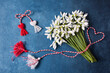 A bouquet of snowdrops flowers and a red and white rope with tassels, a symbol of the arrival of spring on a blue background. Postcard for the feast of March 1 Martisor and Baba Marta