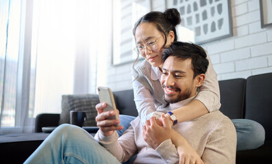 Poster - Phone, love and diversity with a couple in their home, bonding while browsing social media in the living room. Mobile, communication or internet with an interracial man and woman together in a house