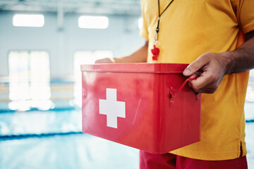 Wall Mural - Box, safety or hands of a lifeguard by a swimming pool helping rescue the public from water danger or drowning. Zoom, trust or man with a medical kit ready for emergency injury support in an accident