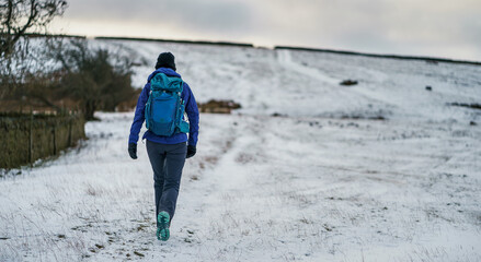 Sticker - A hiker walking up a hill through the snow at Buckshott Fell in winter near Blanchland, Northumberland  in England UK.