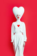 © Uncanny Valley - Creative abstract pastel portrait of a masquerade white costume in the shape of a ghost, spirit of love, a heart shape as a symbol of love and peace. Red background. Illustration. Generative AI.