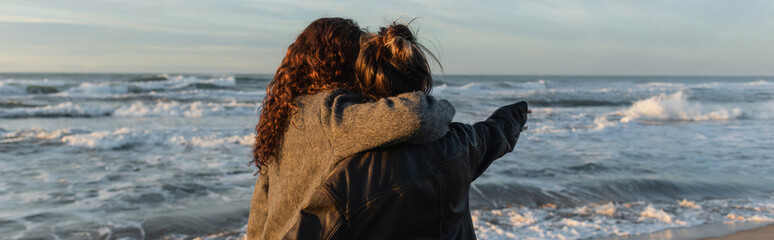 Wall Mural - Back view of woman hugging friend on beach in Barcelona, banner.