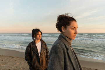 Wall Mural - Young women looking away while standing on beach in Spain.