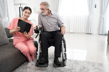 Beautiful doctor take care older caucasian man in electric wheelchair of use tablet computer at home	