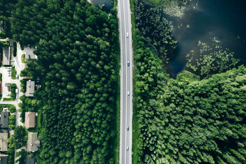 Aerial view of road with cars through green summer woods by blue water lake in Finland.