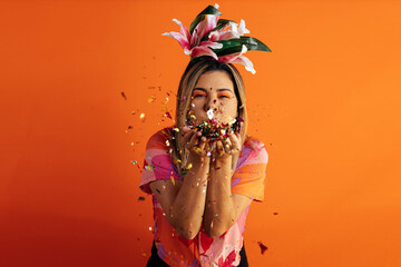 Wall Mural - Brazilian Carnival. Studio shot of young woman celebrating carnival blowing confetti