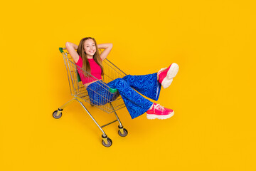 Poster - Photo of positive pretty lady wear trendy clothes hold arms behind head sitting in trolley empty space isolated on yellow color background