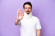 © luismolinero - Young caucasian man wearing neck brace isolated on purple background making stop gesture