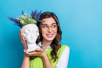 Wall Mural - Photo of pretty minded girl toothy smile arms hold artwork sculpture vase flowers look empty space isolated on blue color background