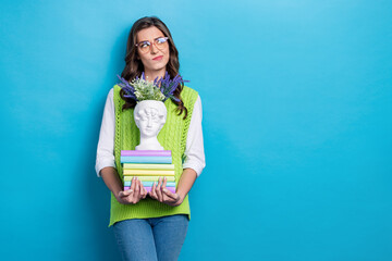 Wall Mural - Photo of minded girl hold pile stack book sculpture vase flowers look empty space hesitate isolated on blue color background