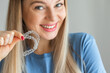 © Ivan - Girl holds transparent braces for dental correction. Person smiling and holding invisible orthodontic retainer and aligner.