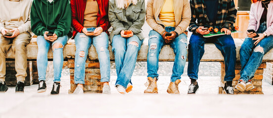 Group of young multiracial friends texting on mobile phone while sitting in the city - Teenagers people having a social network moment watching on their smartphones - Students and telephone concept